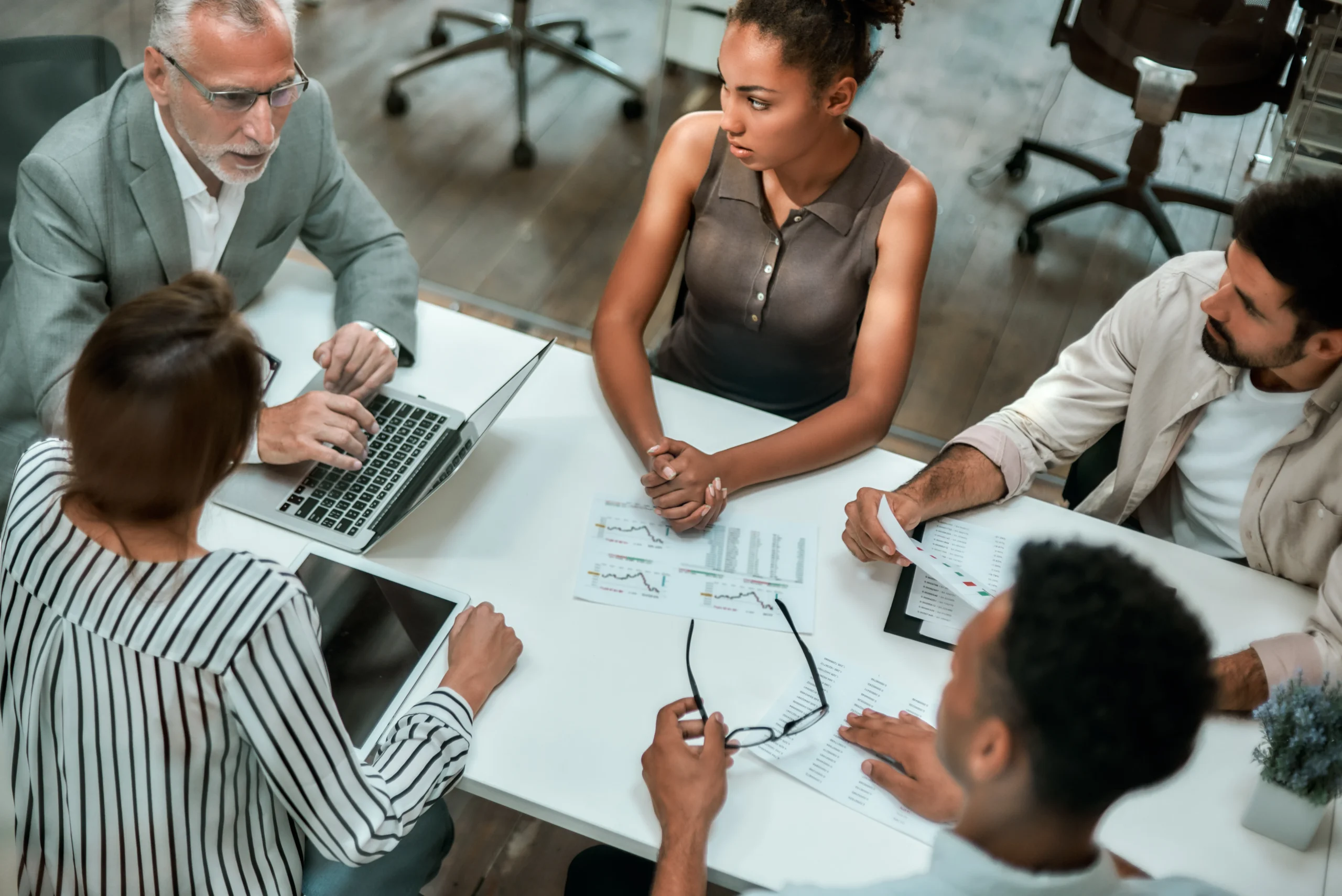 top view of multicultural team discussing business while sitting at the office table together scaled